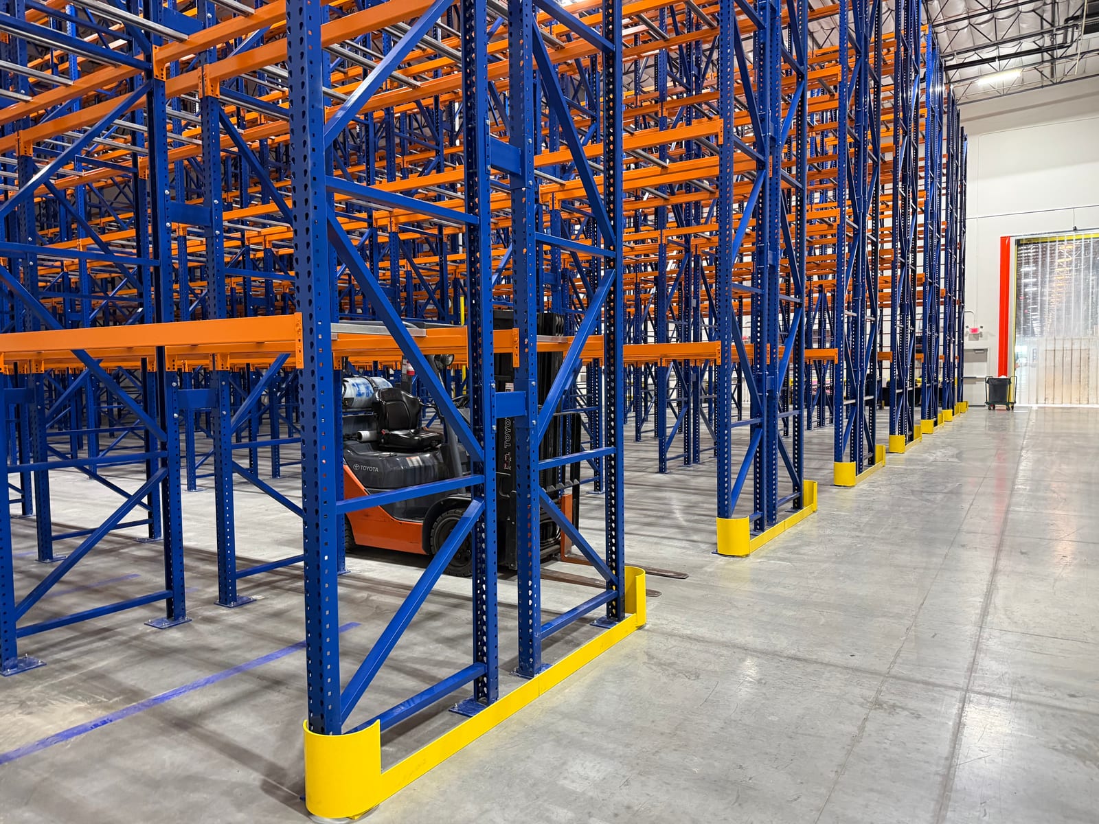 Forklift parked in a pallet rack aisle with yellow end guards protecting the upright frames